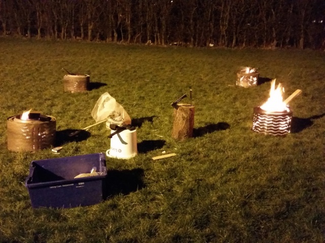 Boxes and buckets are placing on the grass, and fires are burning in the buckets.