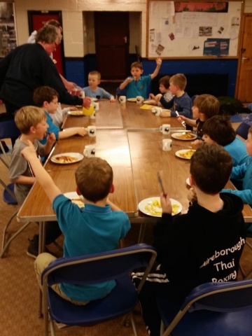 The beaver scouts are having lunch together around a big table.